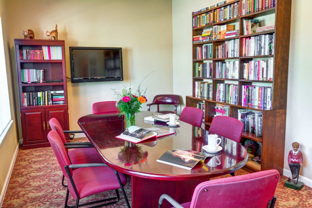 Library and entertainment room with a TV, bookshelves, and long table at Morrow Heights Assisted Living in Rogue River, Oregon