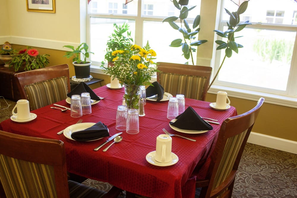 Dining table set with a red tablecloth and fresh flowers at Settler's Park Senior Living in Baker City, Oregon