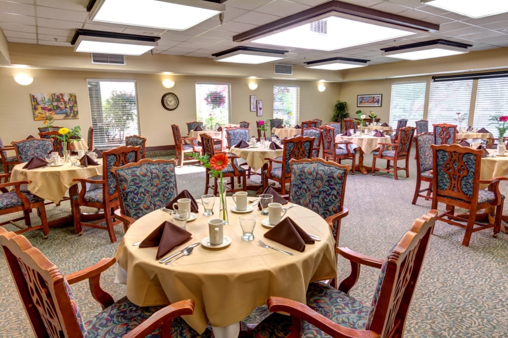 Dining room with tables set with tablecloths and fresh flowers at Silver Creek Senior Living in Woodburn, Oregon