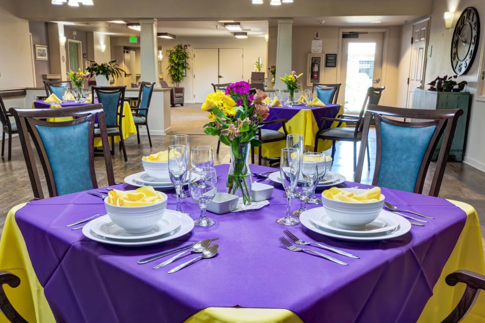 Tables set with tablecloths and fresh flowers in the dining room at Timberwood Court Memory Care in Albany, Oregon
