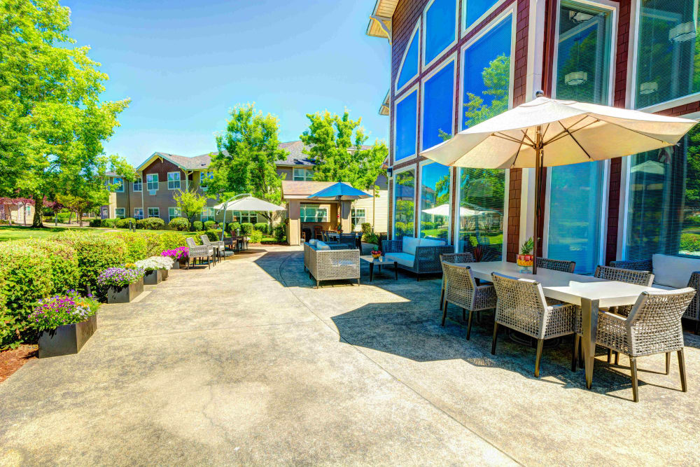 Outdoor lounge seating and patio tables with umbrellas at Vineyard Heights Assisted Living in McMinnville, Oregon
