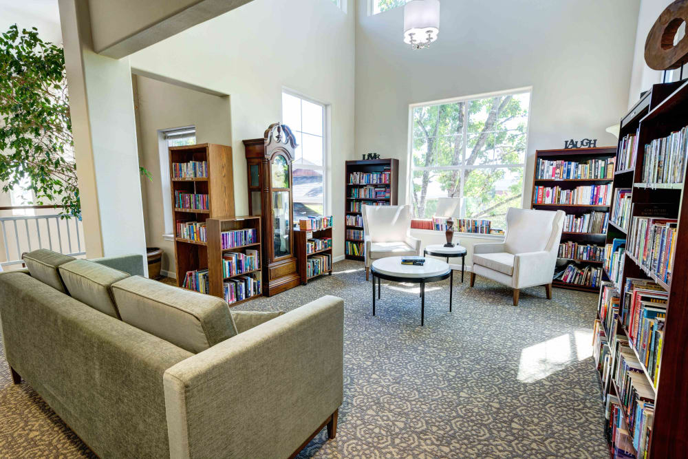 Library with a sofa, armchairs, and large windows at Vineyard Heights Assisted Living in McMinnville, Oregon