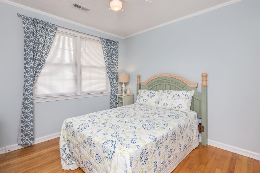 A bed, decorative curtains and wood flooring in an apartment bedroom at Cottage Grove Apartments in Newport News, Virginia