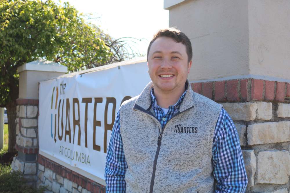 Team member smiling next to sign at The Quarters at Columbia in Columbia, Missouri