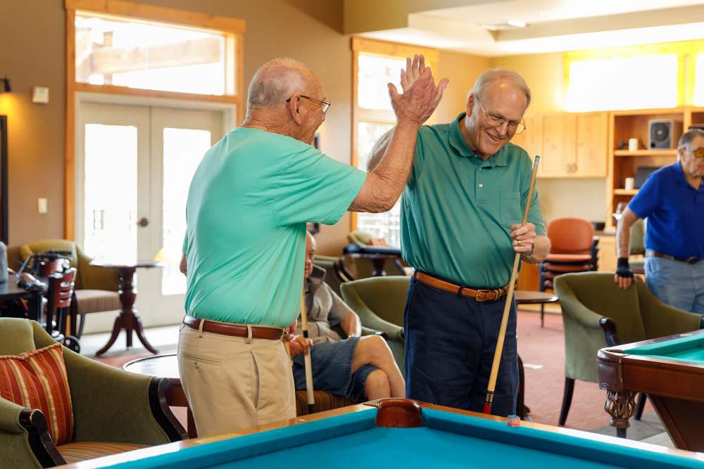 Residents high fiving by a pool table  at Touchmark at Meadow Lake Village in Meridian, Idaho