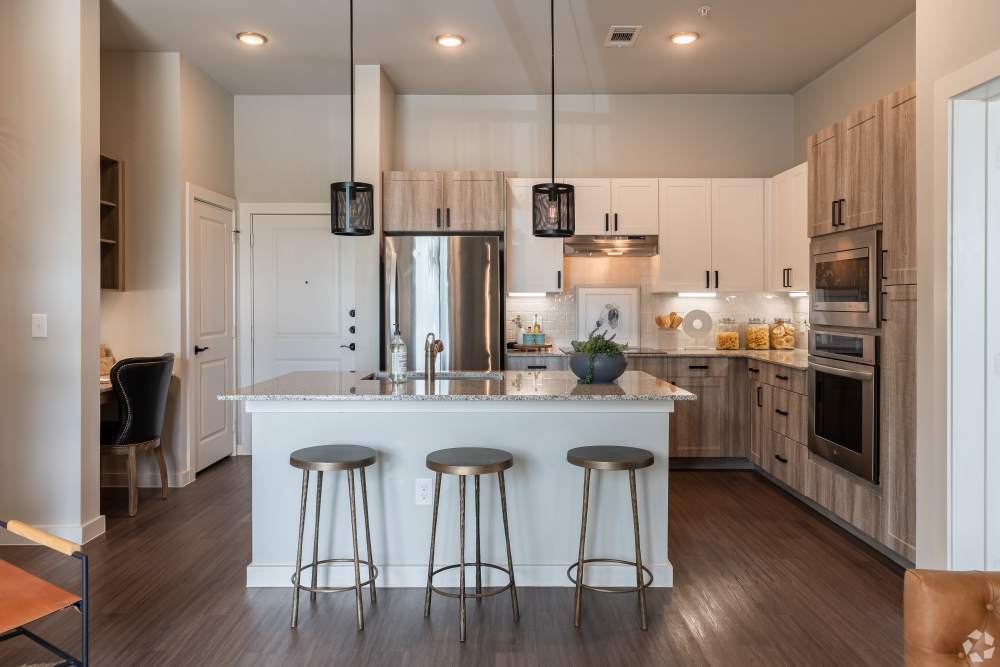 Spacious kitchen with wood floors and island with bar seating in a model home at The Trails at Summer Creek in Fort Worth, Texas