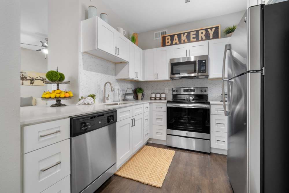 A modern kitchen with sleek stainless steel appliances and a warm wooden floor at Flatiron District at Austin Ranch, The Colony, Texas