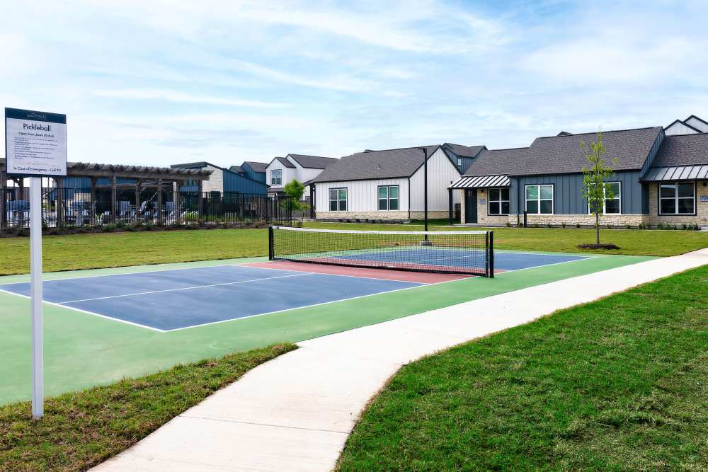 A tennis court with a fence and houses in the background at parcHAUS AT CELINA PARKWAY in Celina, Texas