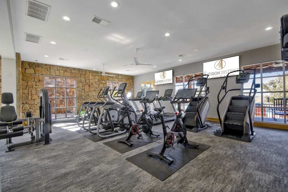 Fully-equipped gym with treadmills, weight machines, and flat-screen TVs at Flatiron District at Austin Ranch in The Colony, Texas