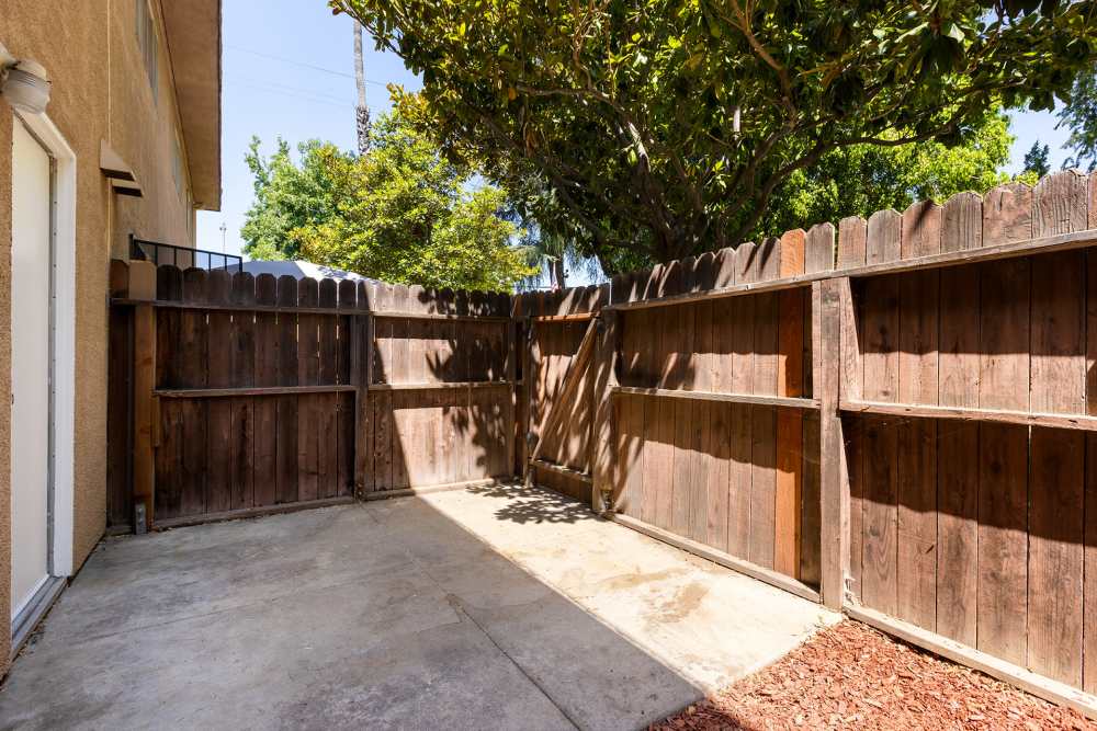  A residential outdoor space with a concrete patio area, reddish-brown mulch ground cover, a tall wooden fence at Reseda Village Green in Reseda, California
