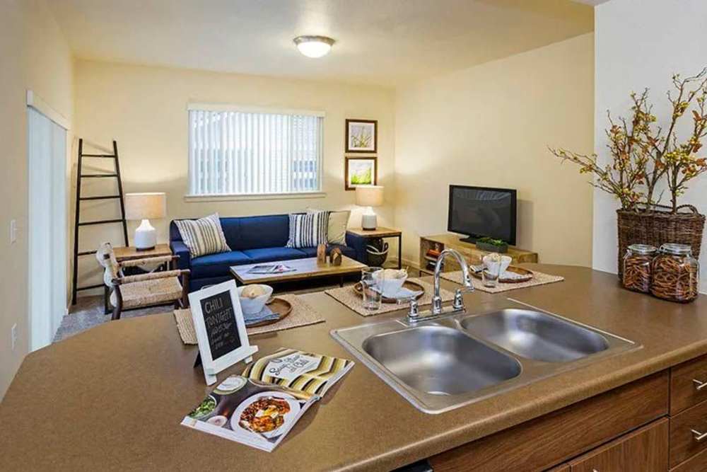 Open-layout kitchen and living room separated by island with waterfall faucet sink at Copper Valley in Puyallup, Washington