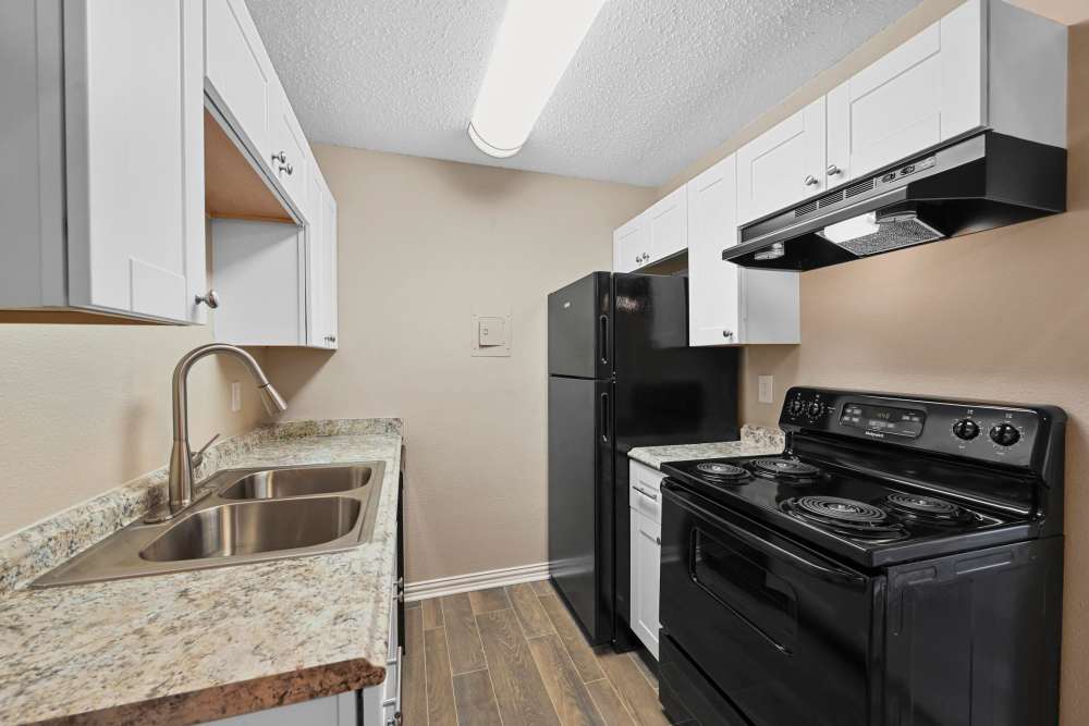 Fully equipped kitchen with granite countertops stainless steel appliances like a refrigerator, stove, and drawer microwave at Village Square in Irving. TX