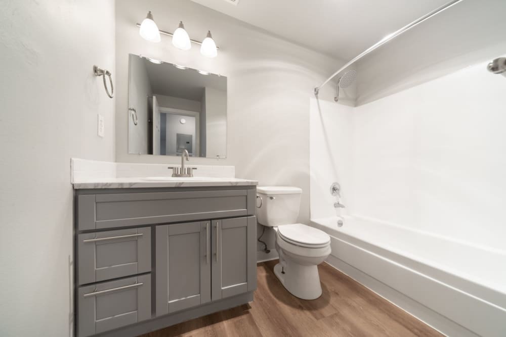 Bathroom with a dark wood vanity cabinet and white countertop, a white toilet and a bathtub with a shower at Lantera Apartments in Seattle, Washington
