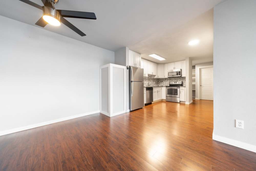 Spacious apartment living room with wood-style flooring, ceiling fan and an open kitchen in the background featuring stainless-steel appliances at Lantera Apartments in Seattle, Washington