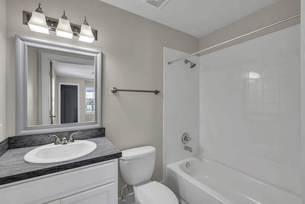 Bright bathroom with vanity light, mirror, commode and standard bath tub at Woodforest Chase in Houston, Texas