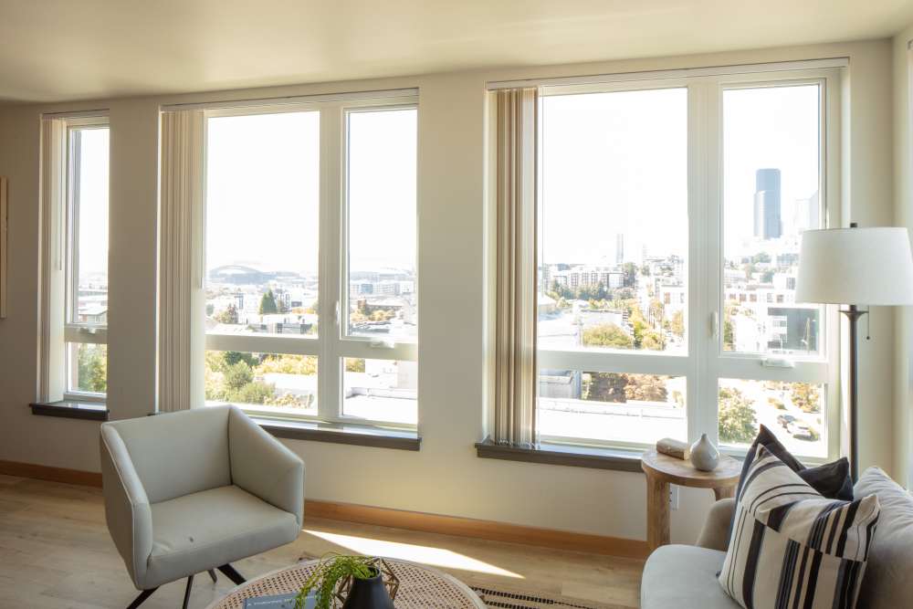 Sun-lit living room with big windows, couches and white lamp at Bryant Manor in Seattle, Washington