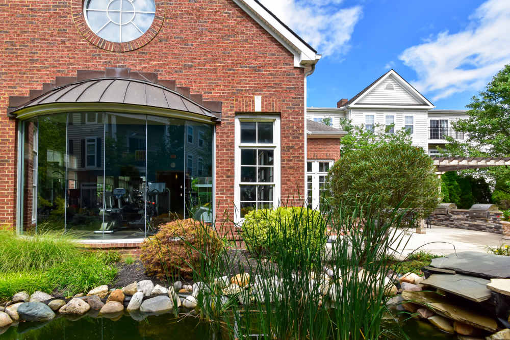 Apartments featuring a rounded glass-enclosed fitness center room and a pond at Central Park Apartment Homes in Columbus, Ohio