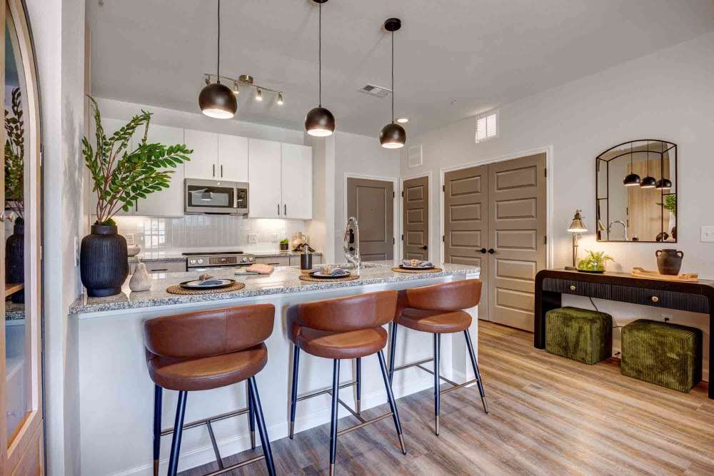 Kitchen island with three brown leather stools in a modern kitchen with granite countertops and white cabinets  at The Abbey at Veramendi in New Braunfels, Texas