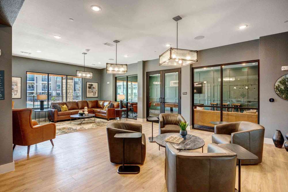  Leather seating is arranged in a modern apartment common area with wood floors at The Abbey at Veramendi in New Braunfels, Texas
