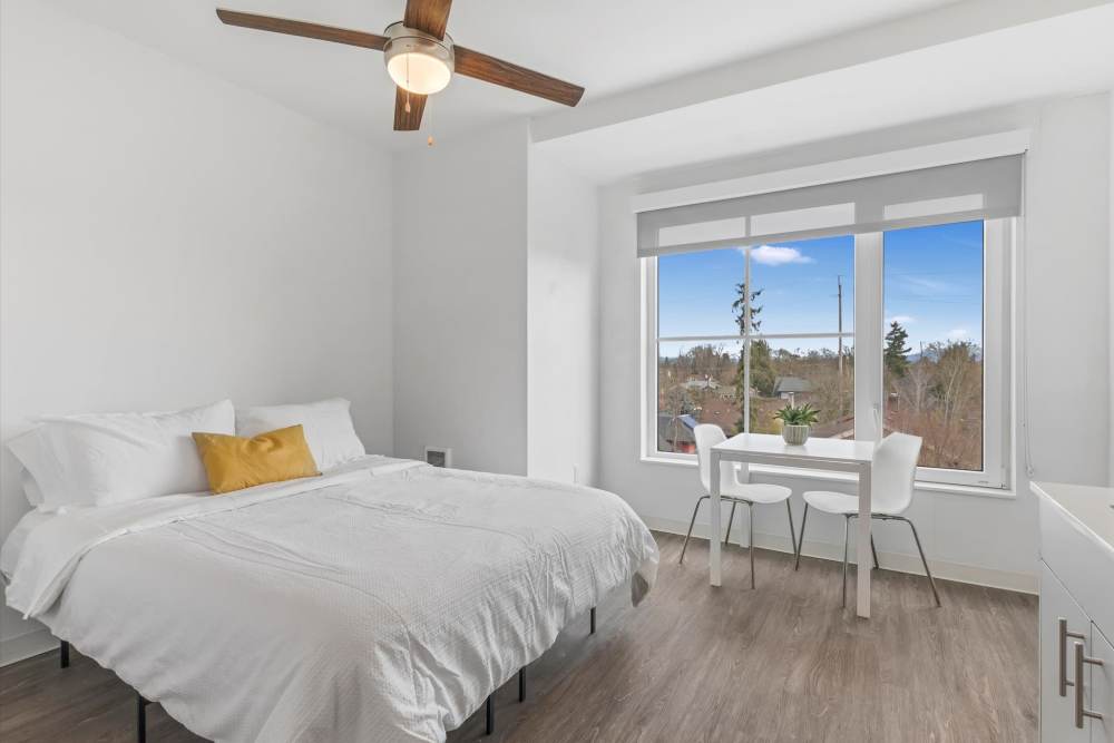 Bright bedroom with a white bed, wood floor, ceiling fan, a small table and chairs and a window at Koz on Killingsworth in Portland, Oregon