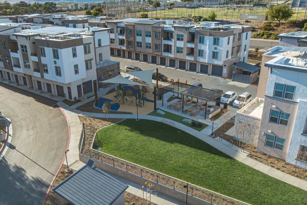 Aerial view of a residential complex featuring a playground surrounded by green spaces and parking areas at Monamos Terrace Apartments in Murrieta, California