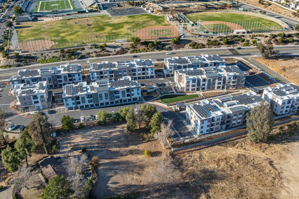 Aerial view of a city residential complex, showcasing multiple buildings and green spaces within an urban environment at Monamos Terrace Apartments in Murrieta, California