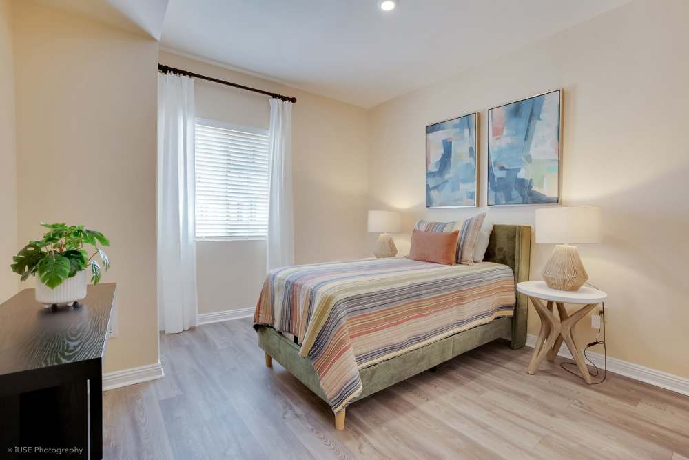 A cozy bedroom featuring a bed, nightstand, and a painting at The Meridian at Boca Raton in Boca Raton, Florida.