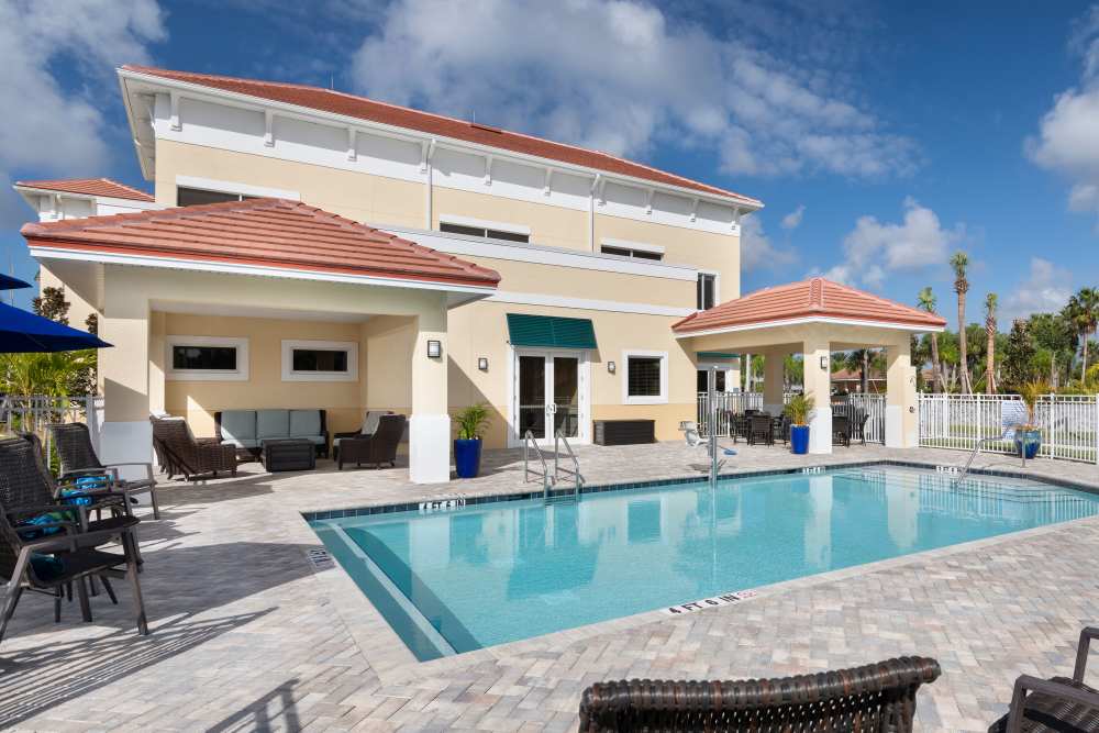 Modern house with red-tiled roof, backyard pool, patio furniture, and palm trees at The Pineapple House at Sapphire Lakes in Naples, Florida