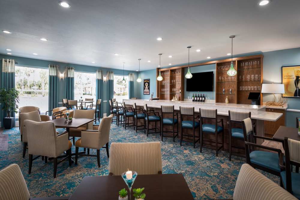 Modern bar and lounge with marble counter, pendant lights, high chairs, and decorative elements at The Pineapple House at Sapphire Lakes in Naples, Florida