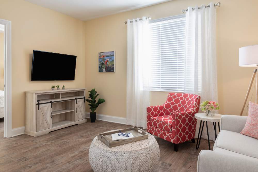 Cozy living room with white couch, red armchair, TV on wall, wooden floor, and light yellow walls at The Pineapple House at Sapphire Lakes in Naples, Florida