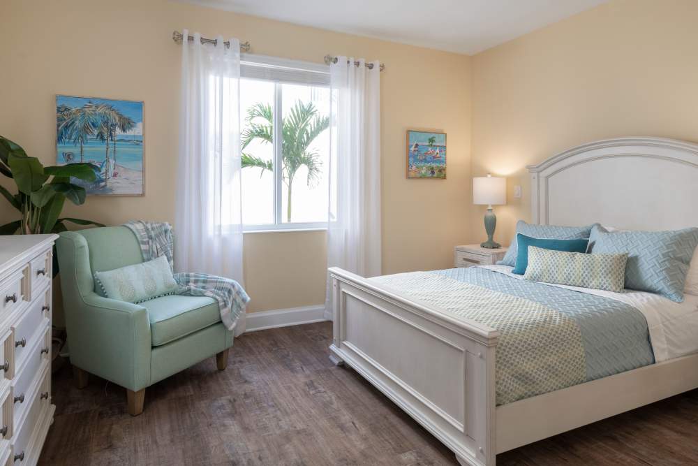 Coastal-themed bedroom with white bed, blue-green bedding, beach art, and wooden flooring at The Pineapple House at Sapphire Lakes in Naples, Florida