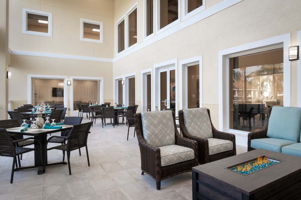 Indoor patio with dining tables, cushioned seating, fire pit table, and large windows for natural light at The Pineapple House at Sapphire Lakes in Naples, Florida