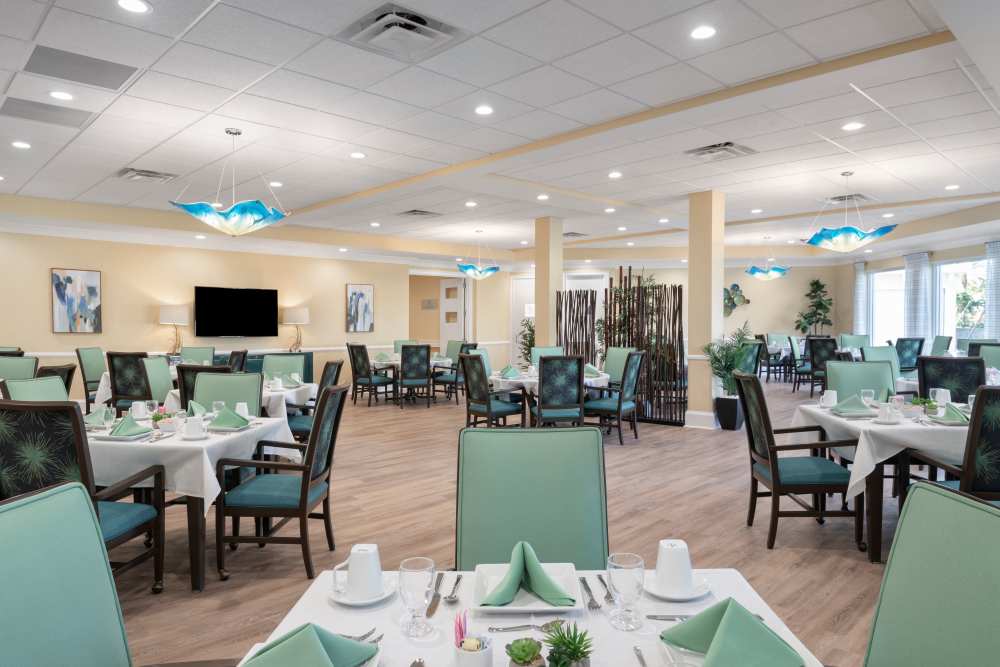 Dining area with white tablecloths, green napkins, pendant lights, and large windows letting in natural light at The Pineapple House at Sapphire Lakes in Naples, Florida