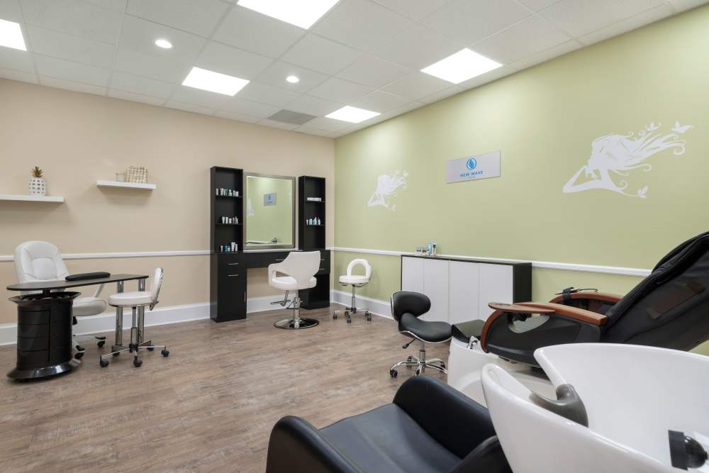 Modern salon with styling chairs, hair-themed wall decals, product shelves, and wooden flooring at The Pineapple House at Sapphire Lakes in Naples, Florida