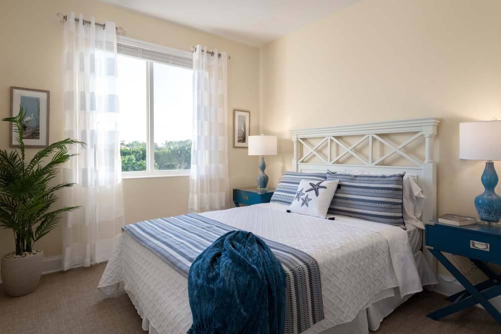 Coastal-themed bedroom with white bed, blue accents, matching nightstands, and a large window with sheer curtains at The Pineapple House at Sapphire Lakes in Naples, Florida