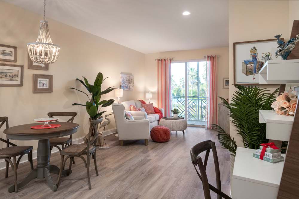 Living and dining area with round table, sofa, desk, large plants, and sliding glass doors to a balcony at The Pineapple House at Sapphire Lakes in Naples, Florida