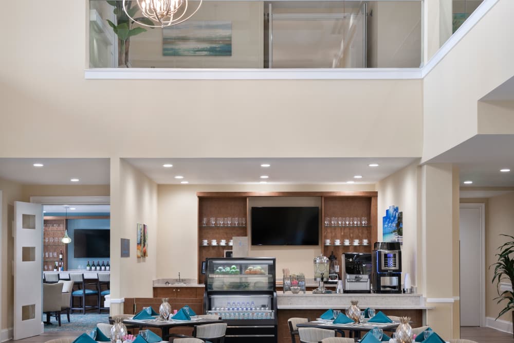 Modern dining area with teal napkins, glassware, counter with coffee machines, and upper level with glass railings at The Pineapple House at Sapphire Lakes in Naples, Florida