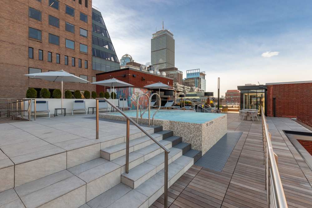 Rooftop patio with outdoor kitchen, grills, dining table, and city skyline under a clear blue sky at 28 Exeter at Newbury in Boston, Massachusetts