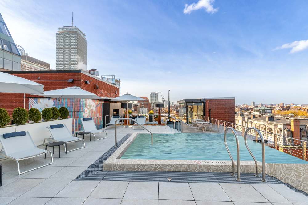 Rooftop pool with lounge chairs, umbrellas, and a city skyline in the background at 28 Exeter at Newbury in Boston, Massachusetts