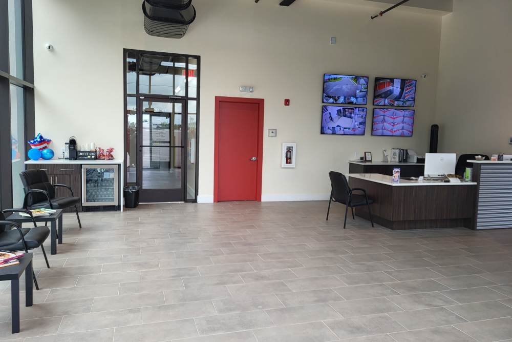 A modern office lobby with black chairs, a coffee station, a red door, security monitors, and a reception desk, at Your Storage Units Clermont in Clermont, Florida.