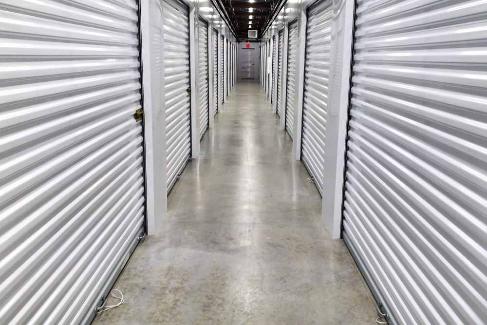 A clean hallway in a storage facility with white roll-up doors on both sides. At Your Storage Units Clermont in Clermont, Florida.
