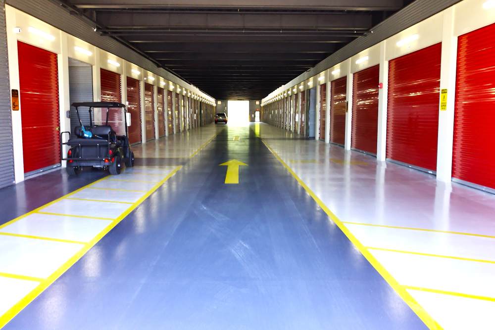 A storage facility hallway with red roll-up doors, yellow floor markings, and a small vehicle parked on the left, at Your Storage Units Clermont in Clermont, Florida.