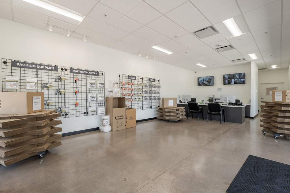 Interior of a packing supplies store with shelves of materials, stacked boxes, and a counter with chairs and monitors