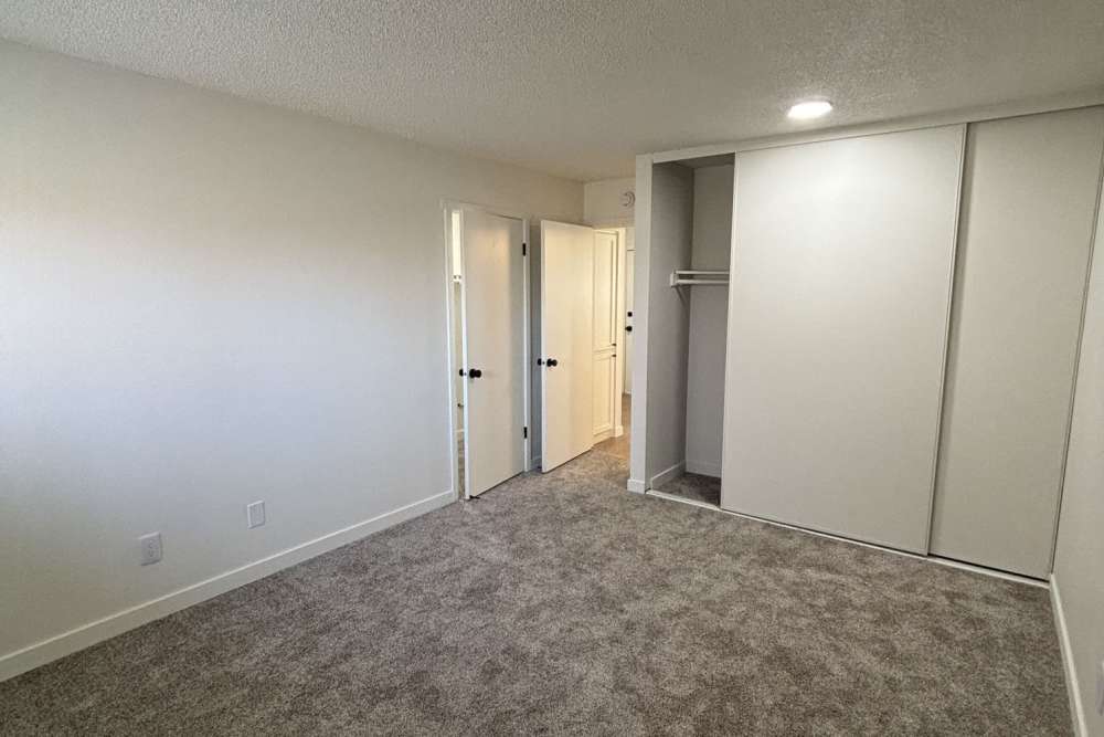 Empty room with beige carpet, white walls, sliding-door closet, and open doorway to another room at Ironwood Greens in Gresham, Oregon