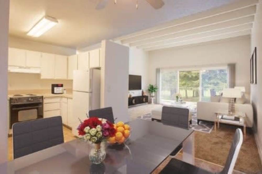 Open-concept space with white kitchen, glass dining table, white sofa, large windows, and wall-mounted TV at Ironwood Greens in Gresham, Oregon