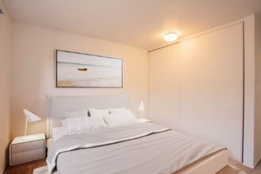 Neat bedroom with white bedding, bedside lamps, framed boat picture, and large closet with sliding doors at Ironwood Greens in Gresham, Oregon