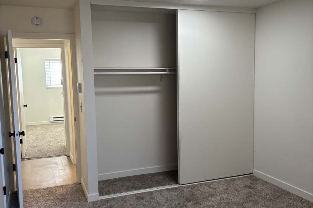 Empty room with beige carpet, white walls, open sliding-door closet, and doorway leading to another area at Ironwood Greens in Gresham, Oregon