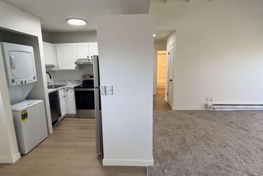Interior view with kitchen, stacked washer-dryer, carpeted living area, baseboard heating, and hallway access at Ironwood Greens in Gresham, Oregon