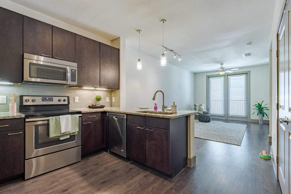 A modern kitchen featuring stainless steel appliances and wood floors at Henley at The Rim, San Antonio, Texas.