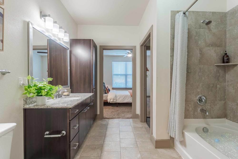 A well-organized bathroom with a sink, bath tub, and cabinets at Henley at The Rim in San Antonio, Texas.